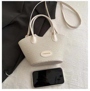 Détail du sac seau tissé crème avec plaque logo dorée et doubles anses souples