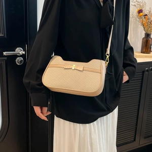 Minimalist beige crossbody bag with woven texture and bow detail worn by a model