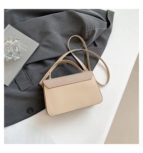 Detail of elegant beige handbag with textured flap on white surface and suit background