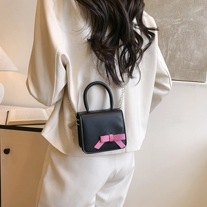 Mini black crossbody bag with pink bow and metal chain strap on model in white suit