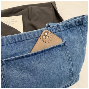 Detail of the front pocket on a denim tote bag, showing phone storage and contrast stitching