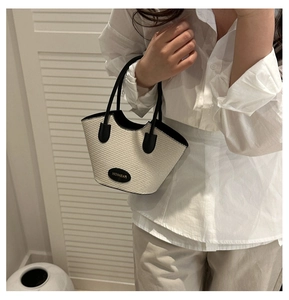 Détail d'un sac seau en paille tissée avec poignées en cuir et écusson logo mode