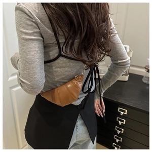 Detail of a mini brown leather croissant crossbody bag with elegant gold chain strap