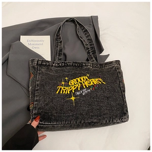 Close-up of acid wash denim tote bag featuring vintage yellow embroidery and star motifs