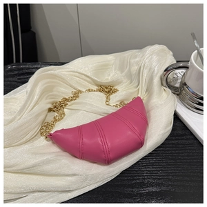 Detail of fuchsia croissant bag with gold chain strap on soft white fabric background