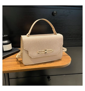 Detail of beige crossbody bag with gold buckle on wooden desk and dark background