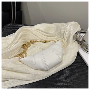 Detailed close-up of white quilted croissant bag with gold chain on soft fabric