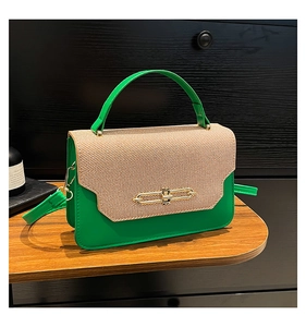 Detail of green leather handbag with woven flap and gold metal clasp on a tray