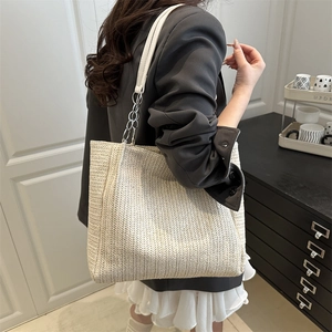 Minimalist beige woven tote bag with chain strap shown on model in a stylish interior