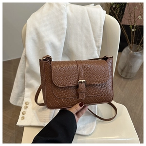 Close-up of brown woven texture and bronze buckle on a stylish crossbody square bag