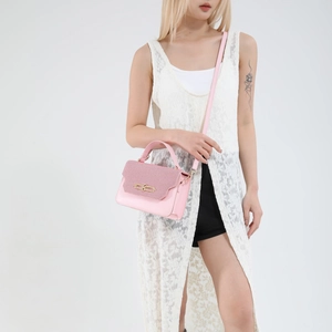 Pink minimalist crossbody handbag with textured flap and gold buckle on a model