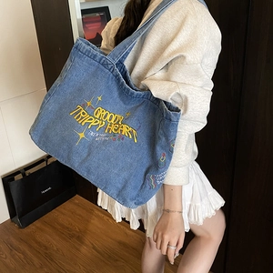 Large denim tote bag with yellow embroidery on shoulder shown on a model in a room