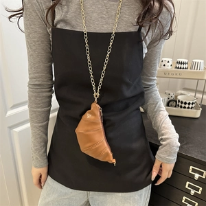 Brown leather crescent mini bag with gold chain strap worn by a model in a modern room