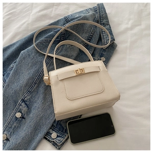 Detail of cream crossbody tote bag with Saffiano texture and gold turn-lock on denim jacket