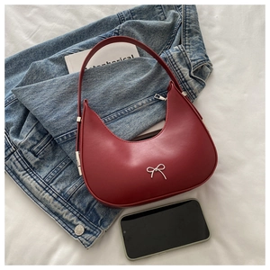 Gros plan du sac demi-lune bordeaux avec nœud argenté et texture de cuir lisse raffinée