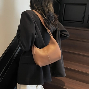 Minimalist brown leather hobo shoulder bag with adjustable strap worn by a model