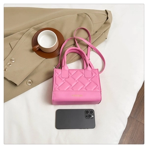 Detailed top view of pink quilted handbag with gold lettering on white fabric