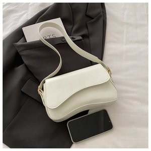 Macro detail of asymmetric white leather saddle bag with gold metal buckle and shoulder strap