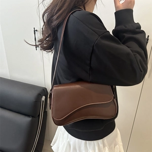 Minimalist dark brown saddle bag with wave-edge flap worn as a crossbody shoulder bag