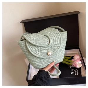 Close-up of light green woven crossbody bag with large pearl button closure in a gift box
