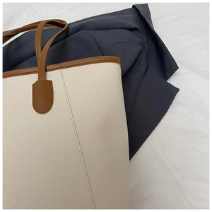 Close-up of beige lychee grain leather tote bag with brown handles and stitching detail