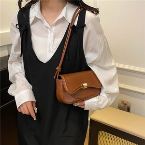Retro brown leather shoulder bag with wavy flap and gold buckle on female model