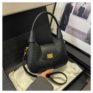 Detail of black crescent bag with woven texture and gold square clasp in a gift box