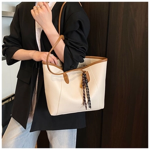 Detail of a beige pebbled leather tote bag with brown straps and striped silk scarf accessory
