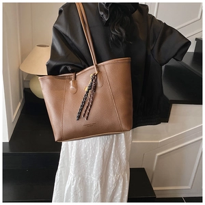 Close-up of brown litchi pattern leather tote bag with woven tassel charm and shoulder straps