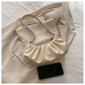 Detail of beige pleated cloud bag with metallic clasp on a stylish cream blazer
