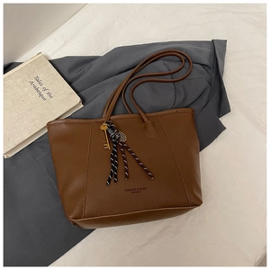 Detailed macro view of brown lychee grain leather tote bag with gold key and fringe charm