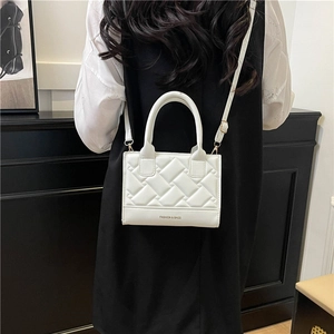 White quilted crossbody bag with top handle and adjustable strap worn by model