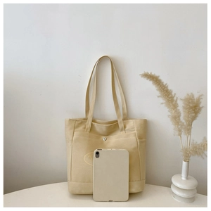 Canvas tote bag detail showing exterior pocket with metal buckle and iPad size comparison