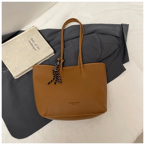 Detail of a brown textured leather tote bag with braided charm and wide base for capacity