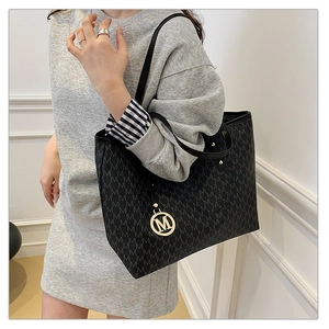 Detail of black tote bag with 'M' letter print and gold logo pendant on leather handle
