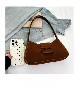 Miniature brown suede shoulder bag with bow detail compared to a phone for size scaling
