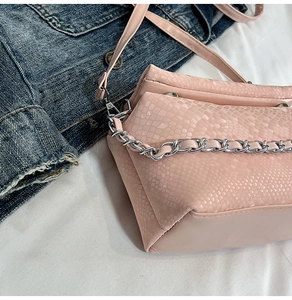 Detail of pink faux snakeskin handbag with silver chain on denim jacket background