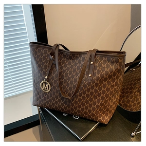 Detailed view of the dark brown tote bag with M-logo pattern and golden charm