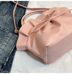 Close-up of pink ruched cloud bag with bow detail on white cloth and denim jacket