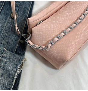 Detail of pink snake-embossed bag with silver metal chain strap on denim jacket