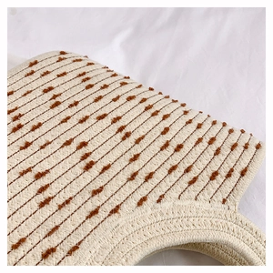 Detail of beige woven straw bag featuring brown tufted dots and boho textile texture