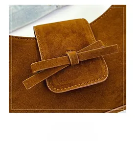 Detailed view of brown suede shoulder bag featuring a flat bow ornament and fine stitching