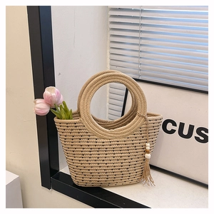 Detail of woven straw tote bag with round handle and tassel accessory for summer beach
