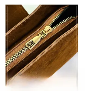 Close-up of golden metal zipper on a dark brown suede leather minimalist handbag