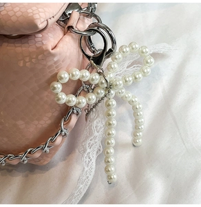 Detail of pink snake-pattern box bag with pearl bow charm and silver chain strap