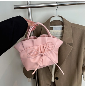 Close-up of pink pleated cloud bag featuring ribbon bow and subtle butterfly pattern
