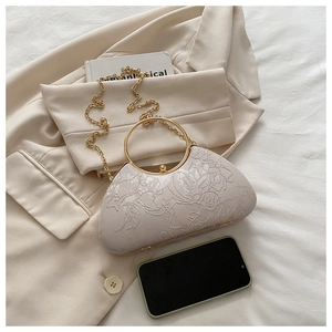 Close-up of floral embroidery on a beige handbag with a gold ring handle and metal clasp