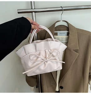 Detailed close-up of a soft pink ruched handbag with a decorative oversized leather bow