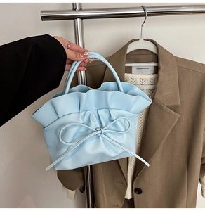 Detail of light blue pleated handbag featuring a delicate matching bow and soft texture