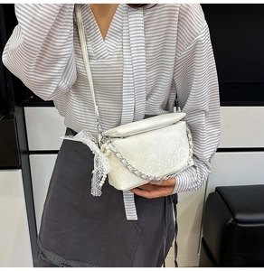 Close-up of white crocodile texture crossbody bag with silver chain and lace bow detail